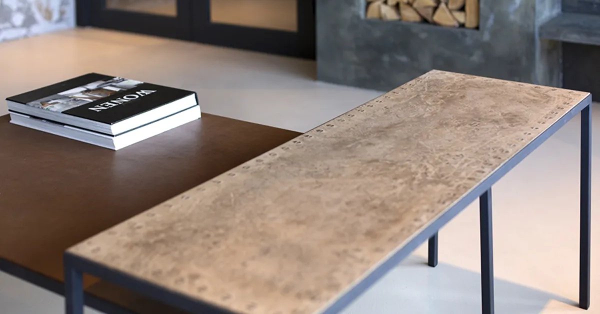 Interieur met een langwerpige tafel met steenachtig blad en een ruwe grijze wand met houtnis.